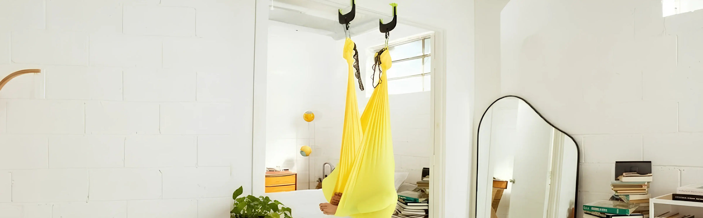 Woman using yellow aerial yoga hammock in doorway, practicing indoor stretching, balance and relaxation in bright home fitness space daily sessions